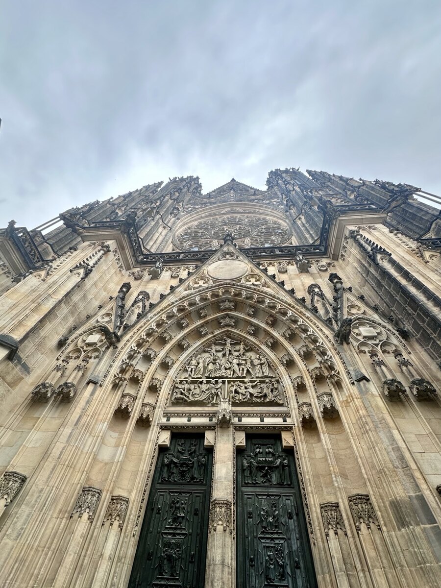 An upward view of St. Vitus Cathedral’s carved stone doorway and rose window in Prague, Czechia